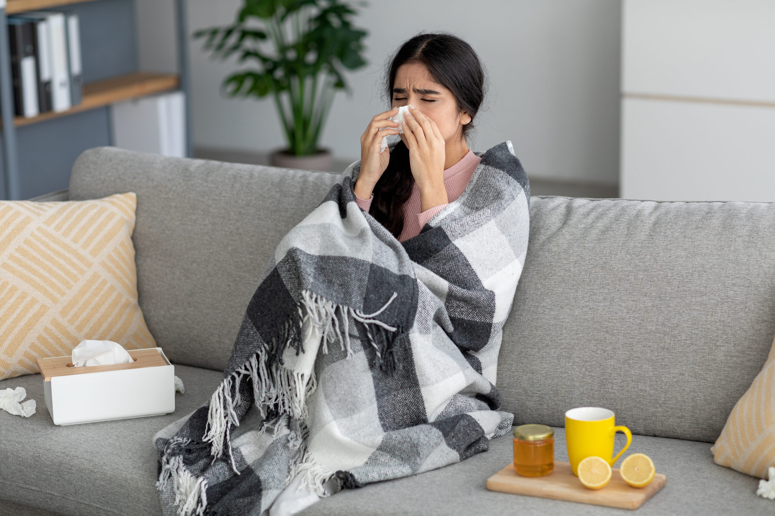 A woman is stuck inside with a runny nose and chills, common symptoms of the cold and flu.